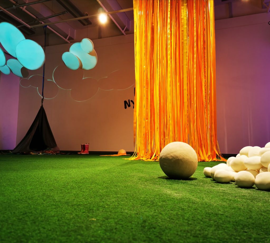Kuvassa osa Mistä nyt tuulee? näyttelystä. Näyttelyn nauha-aurinko, vihreä matto, kumisaappaat, lumipalloja ja lumilapio.