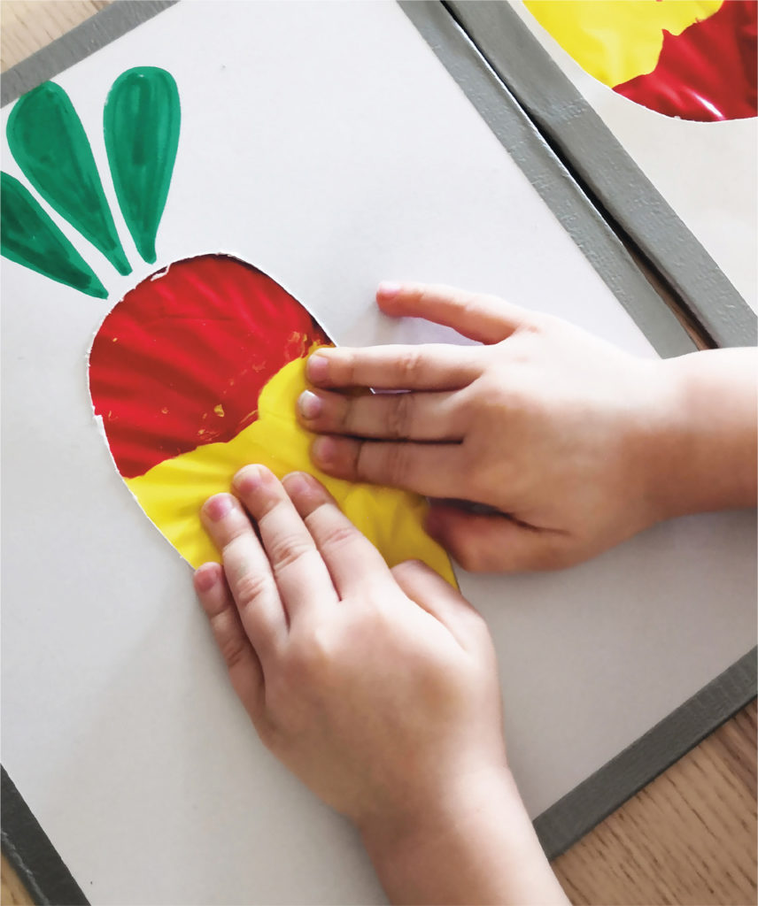 Lapsi tekemässä sotkutonta maalausta. Kuvassa lapsen kädet painamassa muovipussia, jonka alla on väriä.
