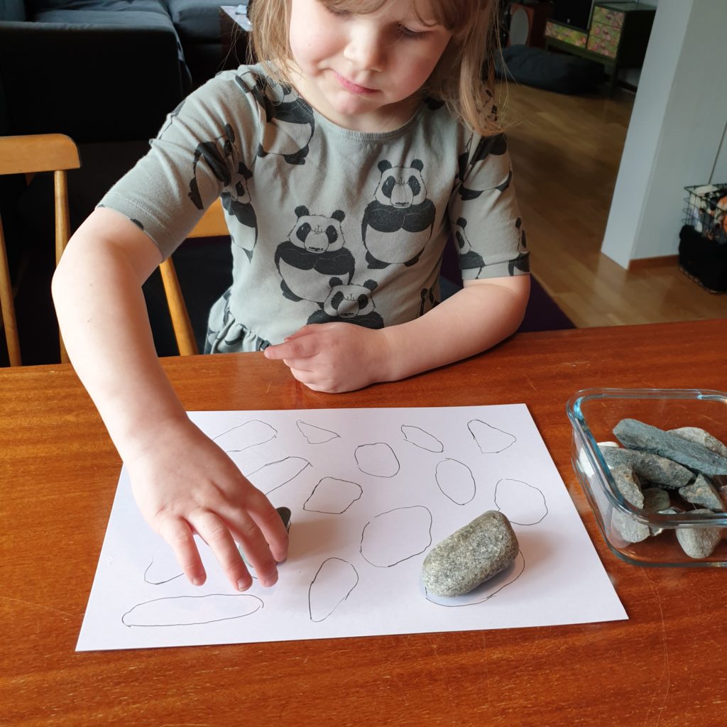 Kuvassa lapsi asettelee eri kokoisia kiviä paperille.