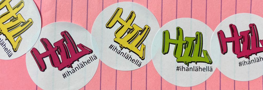 Vihreitä, keltaisia ja pinkkejä HIL-logoja vaaleanpunaisella paperilla