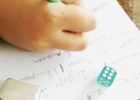 Kuvassa lapsi kirjoittaa runoa valkoiselle paperille. Vieressä pyyhekumi ja noppa.