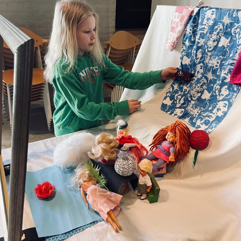 Tyttö asettelee nukkeja ja kankaita kuvaan taidemuseon työpajassa