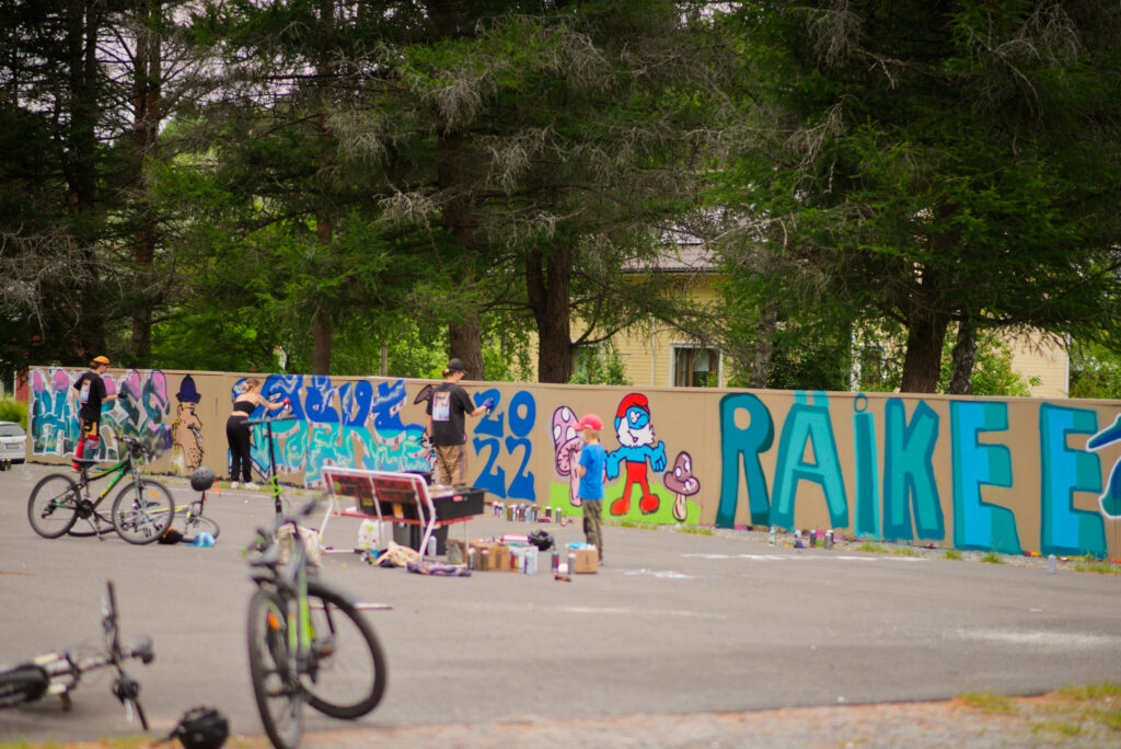 Graffitimaalareita maalausseinällä. Iso, maalattu teksti: Räikeee