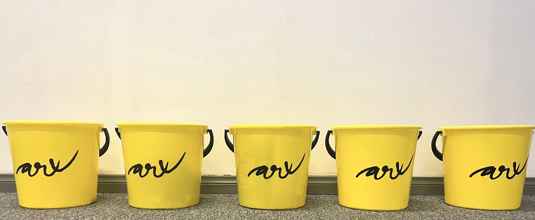 Rivissä 5 keltaista muoviämpäriä, joissa musta ARX-logo