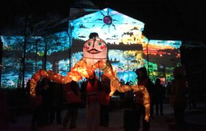 Valoilmiö-festivaali 2025. Etualalla jättiläisvalonukke Kristiina, taustalla kirkko, jossa Alexander Salvesenin Lastemme perintö -projisointi.