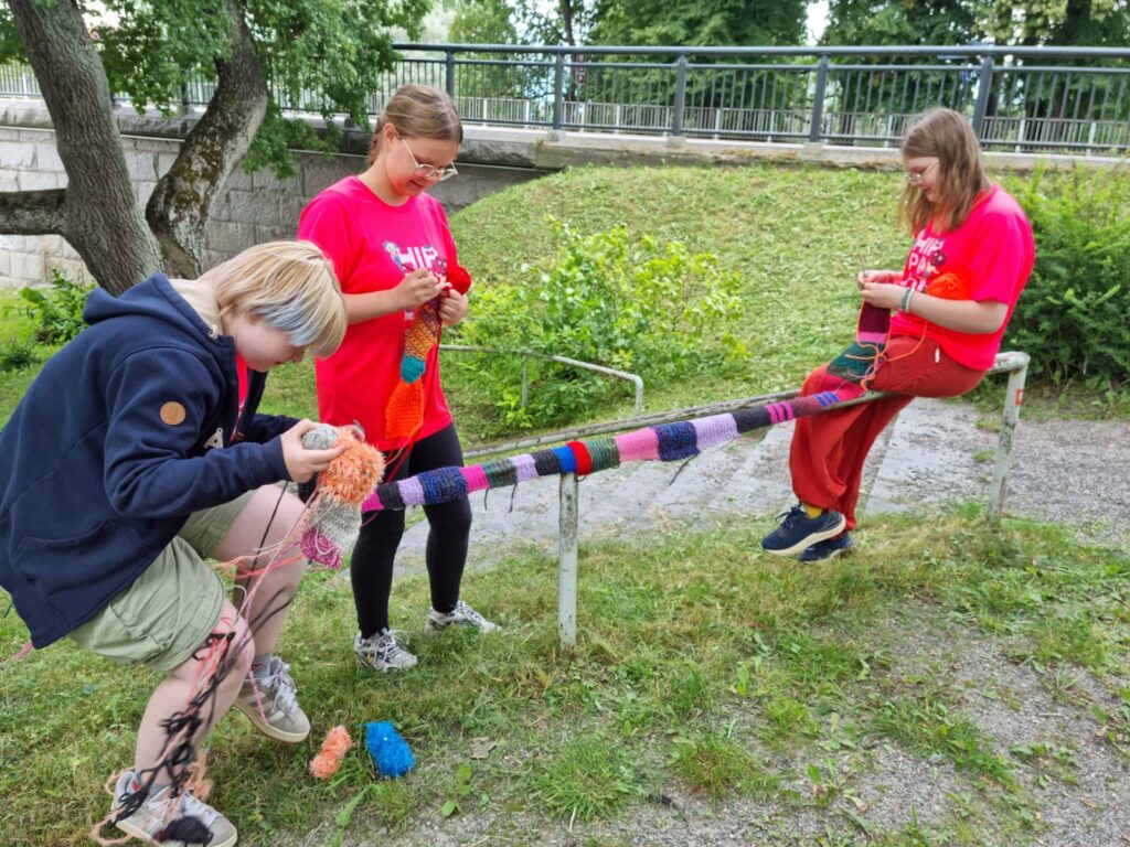 Kolme nuorta tekee neulegraffitia virkaten ja neuloen